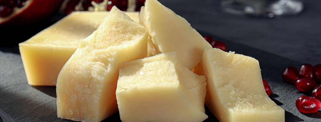 Thick parts of cheese served on a plate in front of a dark background with pommegranat seeds sprinkled around