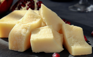 Thick parts of cheese served on a plate in front of a dark background with pommegranat seeds sprinkled around