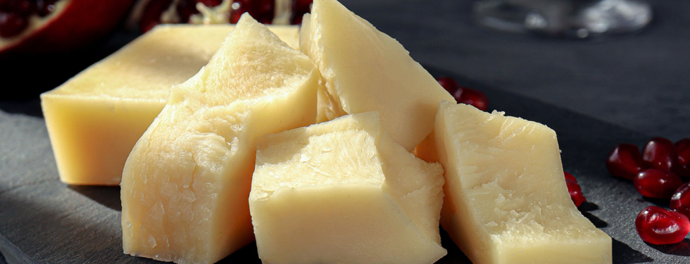 Thick parts of cheese served on a plate in front of a dark background with pommegranat seeds sprinkled around