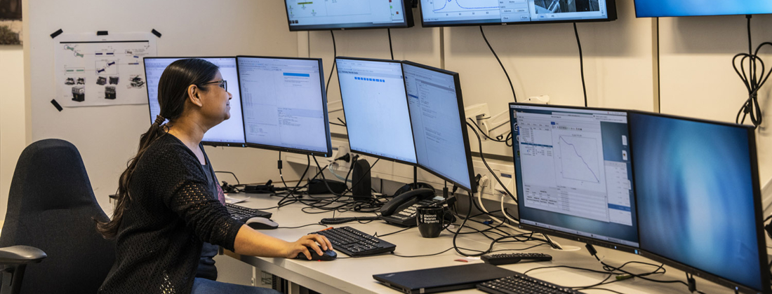 Female researcher sitting in front of a desk and many large screens in a control room at MAX IV.