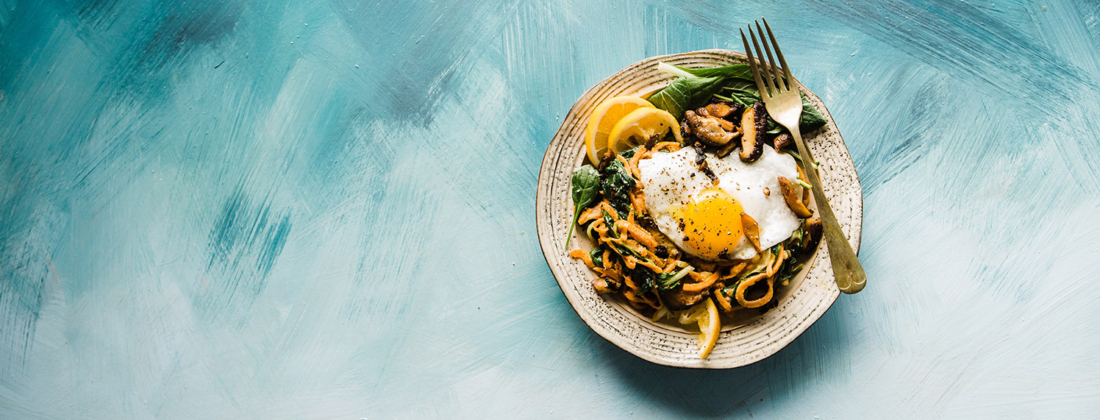 Food plate on white and blue table containing fried eggs and vegetarian ingredients