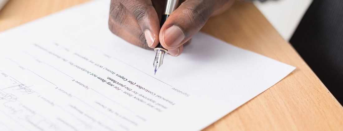 Hand holding a pen signing a contract paper lying on a table.