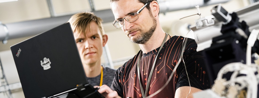 Two male scientists at MAX IV standing in front of a laptop with focused facial expressions.