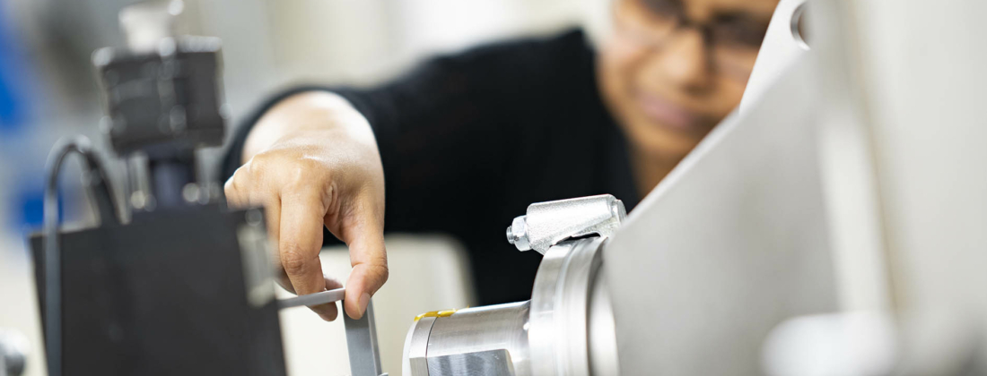 Woman bending forwards focusing her hand on part of a beamline at MAX IV.