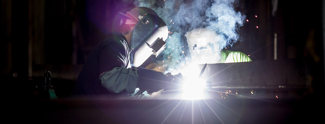 Dark image showing a manufacturer with a mask working with metal welding