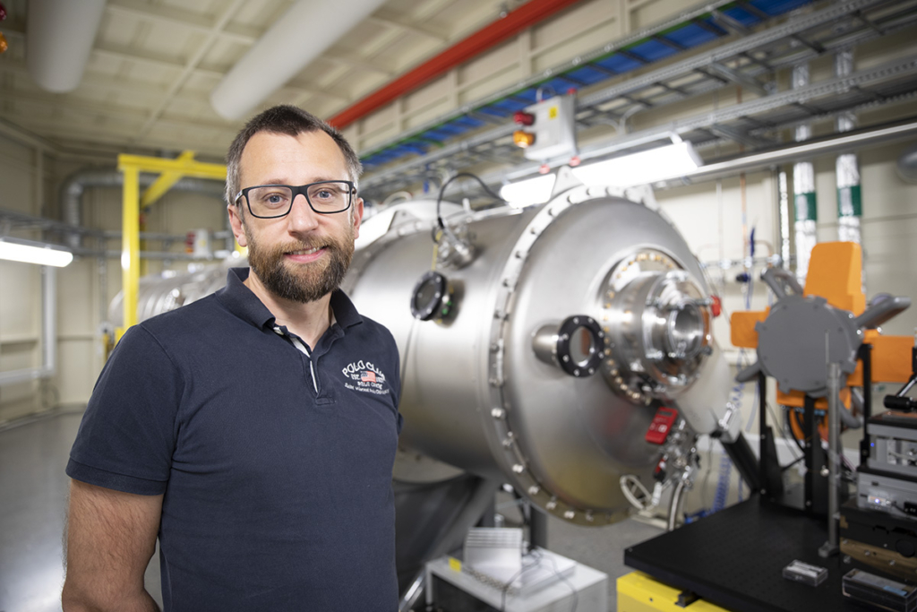 Portrait of middle-aged man with glasses and dark shirt in front of beamline at MAX IV.