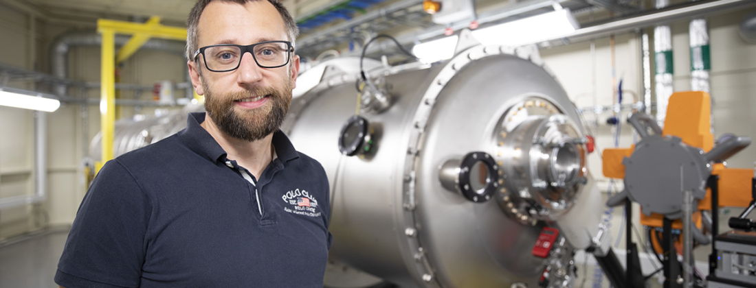 Portrait of middle-aged man with glasses and dark shirt in front of beamline at MAX IV.