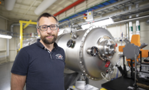 Portrait of middle-aged man with glasses and dark shirt in front of beamline at MAX IV.