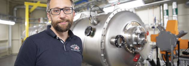 Portrait of middle-aged man with glasses and dark shirt in front of beamline at MAX IV.