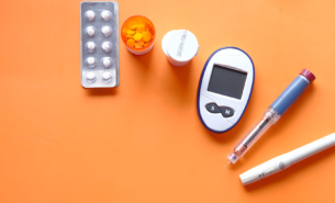 diabetes device for measuring blood sugar levelsand tablets on orange background