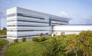 Image of the external MAX IV building with a focus on the office building, trees and green hills in the surroundings.